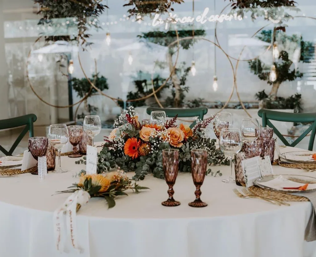 Mesa de banquete vestida con centro floral en tonos naranja y cristalería